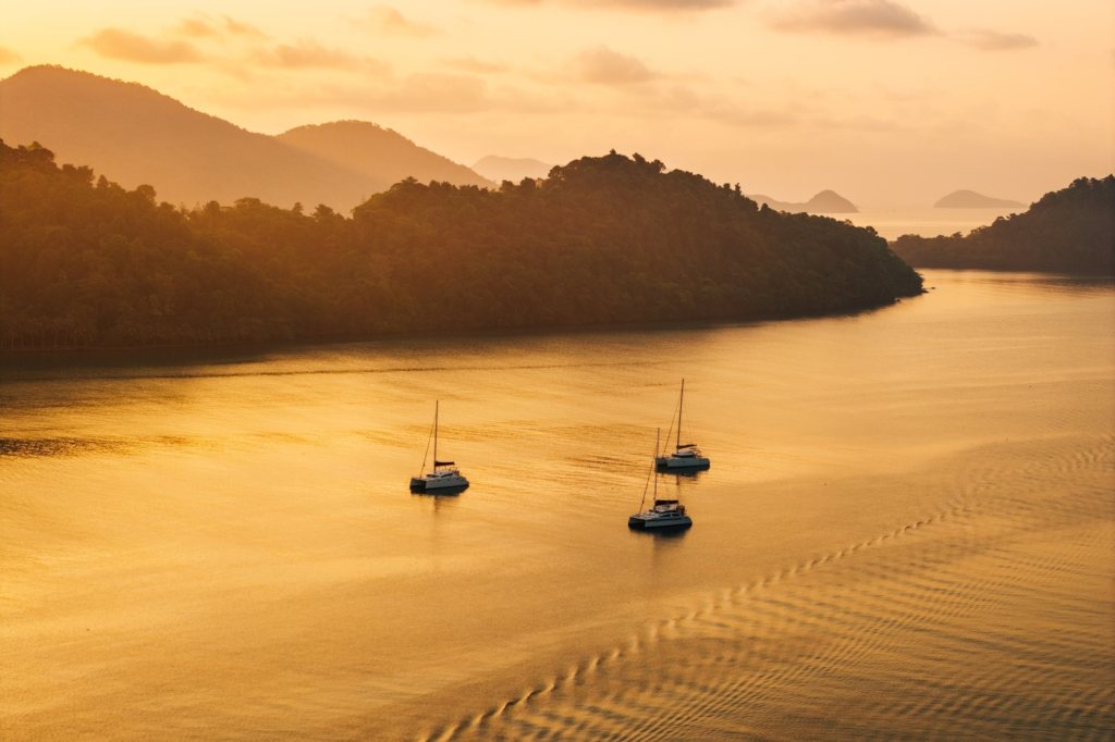 Yachts anchored in calm water at golden hour surrounded by tropical islands