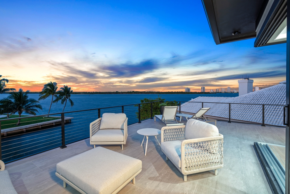 Luxury waterfront terrace with elegant outdoor seating overlooking the ocean at sunset.